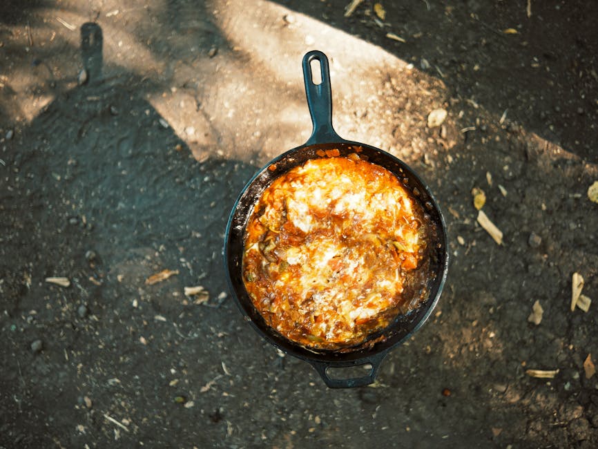 Delicious stew cooking in a cast iron skillet over open fire outdoors, perfect rustic meal.