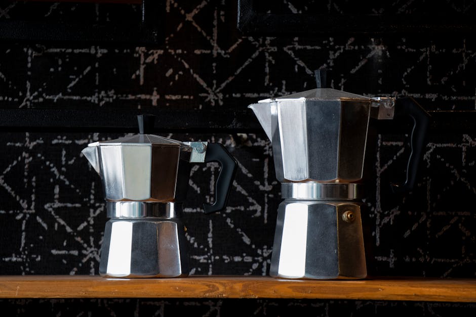 Stainless steel Moka pot surrounded by coffee beans and espresso cup on marble countertop with morning light