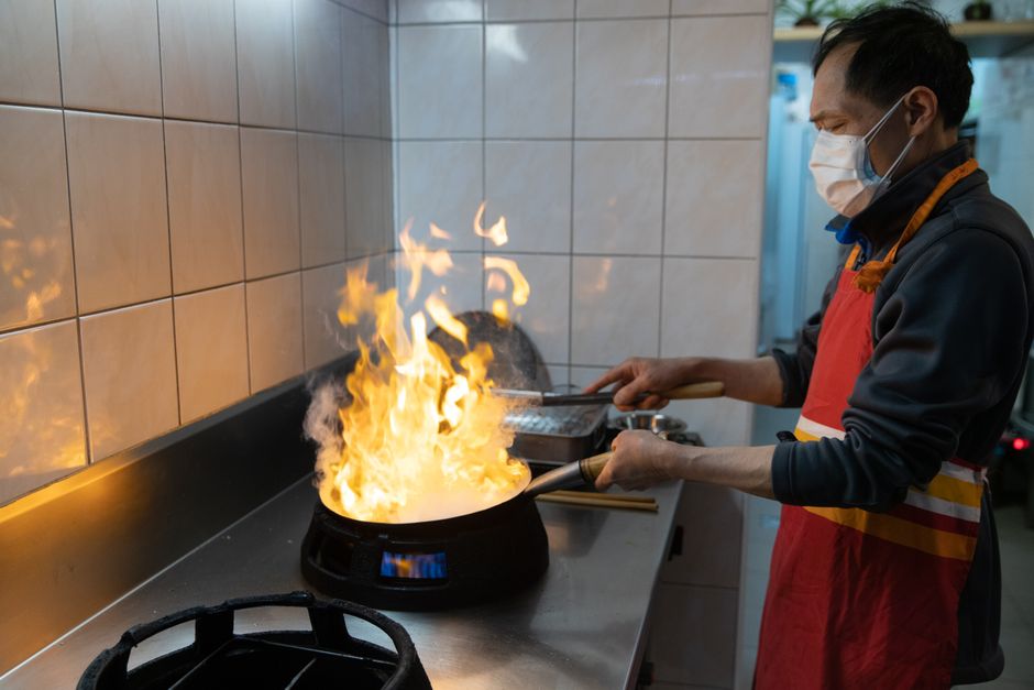 Carbon steel wok on electric coil burner and induction cooktop side-by-side comparison with sizzling oil and steam